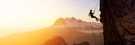 A rock climber on a rope hanging off a cliff