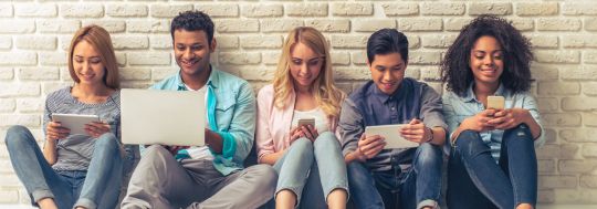 Five people sitting on the ground leaning against a wall