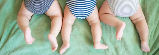 Newborn triplets lie on a stomach on a blanket