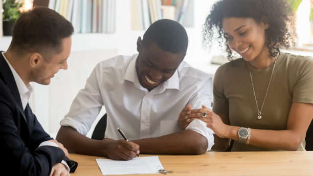 A man and woman sign a contract, watched on by a man in a business suit. | Canstar