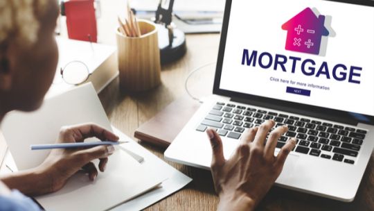 A woman types on a laptop computer with the screen showing an online mortgage signup