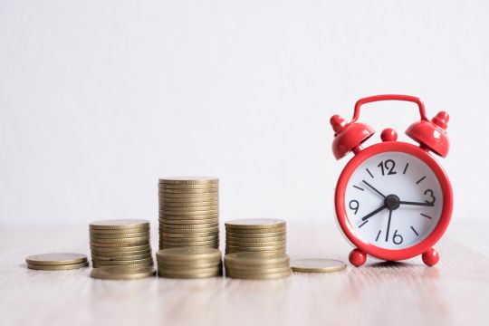 Red alarm clock next to a pile of stacked coins