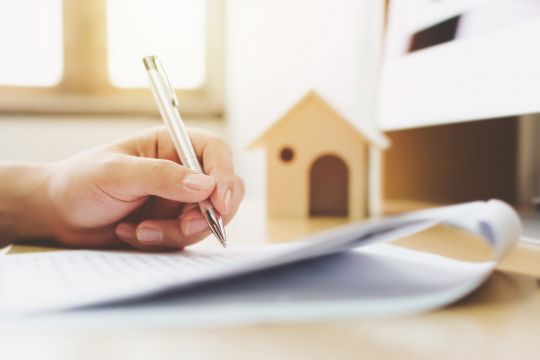 Person signing document with model house in background