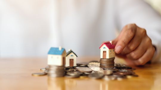 Closeup image of a woman's hand putting house model on pile of coins for saving money concept