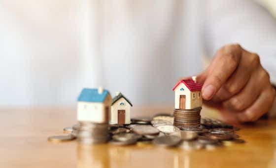 Closeup image of a woman&#8217;s hand putting house model on pile of coins for saving money concept