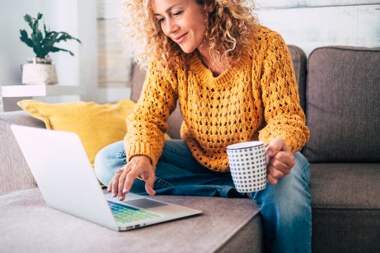 Woman sitting on couch with coffee researching on laptop