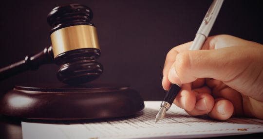 Someone writing on a piece of paper with a fountain pen, and there is a gavel next to it
