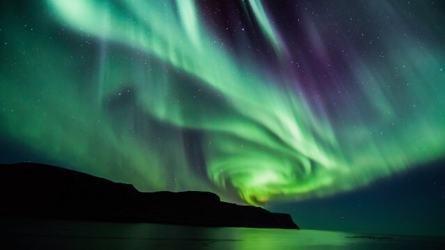 Bright green rays of the Aurora Borealis, twisted into a spiral, shine over Iceland