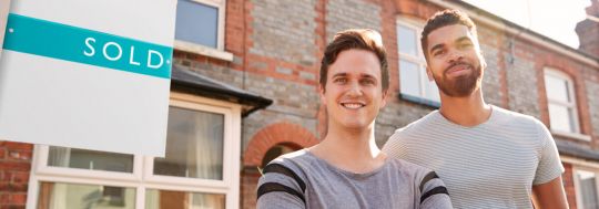 Two men standing in front of a sold sign and a property