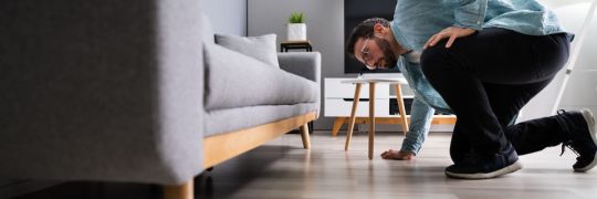 A young man searching for an item under his couch
