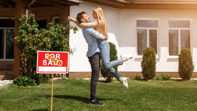Young couple outside a home with a sold sticker on the For Sale sign.
