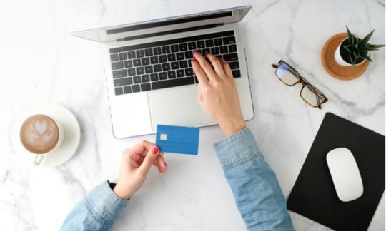 A woman holds a blue credit card while typing on her laptop representing Low income credit cards.