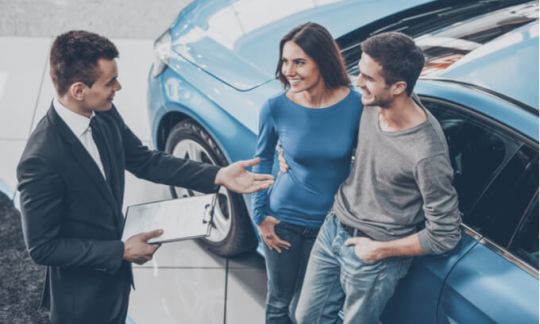 A couple leaning against a car talking to a car salesman. Can you transfer a car loan to someone else?