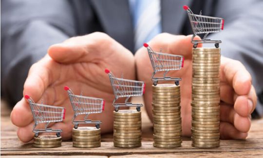 Increasing piles of coins each with a miniature shopping trolley on top