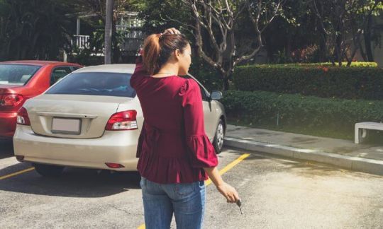 Woman standing in a car park holding her keys, looking at an empty car park space