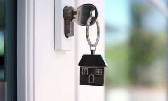 Key in a door with a keyring in the shape of a house