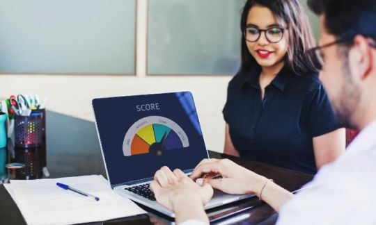 Two people sitting at a desk looking at a credit score on a laptop