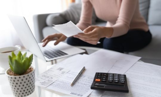 A woman with a laptop and calculator checking her finances