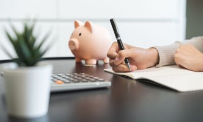 A woman writes notes in a notebook about her super fund with a small piggy bank in the background.