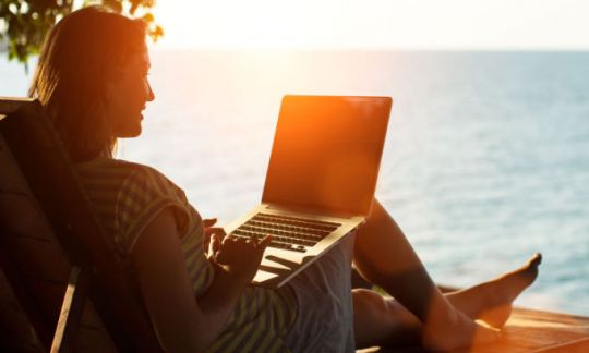 A woman with her laptop relaxing at sunset