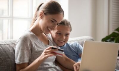 A mother and son sit on the couch looking at a laptop representing at what age should I give my child a debit card.