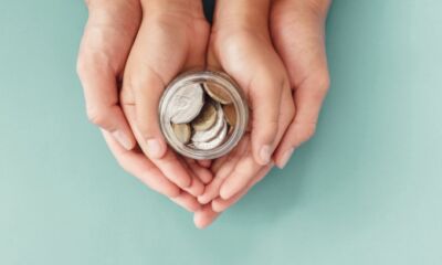 A parent supports their child's hands as they hold a jar of coins.