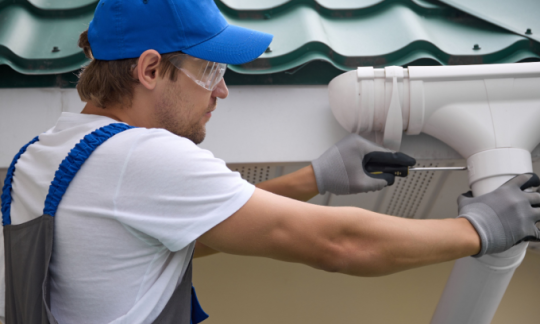 A professional installs guttering and contemplates gutter replacement cost.