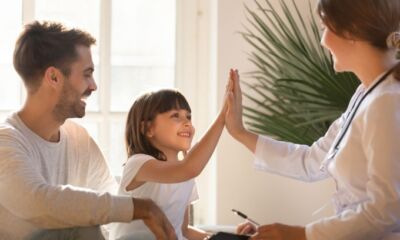 A young daughter hi-fives a female doctor while sitting next to her father representing health insurance deals.