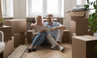 An older couple sits on the floor surrounded by boxes representing home loans for pensioners.