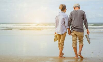 An older couple walking on the beach thinking about how much do I need to retire on $100,000 a year.
