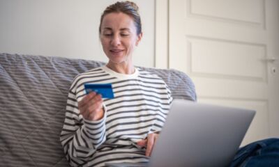 A woman in a stripped shirt looks at her credit card with her laptop on her lap representing how to increase credit card limit.