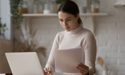 A woman holds some documents while looking at her laptop representing reportable employer superannuation contributions.