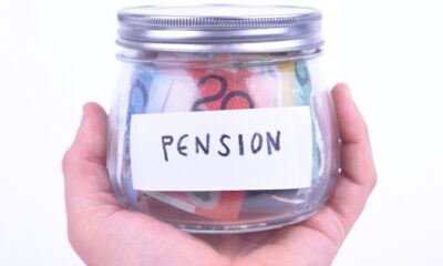 A hand holds a glass jar with the word "pension" written on white tape on its front, with Australian dollar notes inside representing reversionary pension.