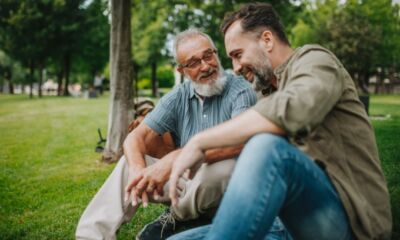 An elderly father sits next to his adult son at a park.
