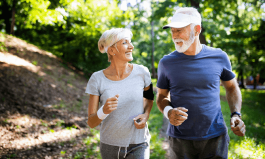An elderly woman and man jogging in the outdoors on a sunny day
