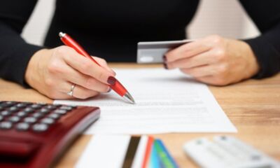 A woman holds her credit card while looking over the terms and conditions of the card representing credit cards fees.
