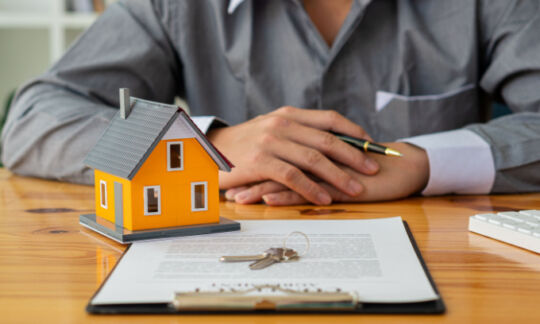 A man sits in front of a model house representing what is title insurance and is it worth it?